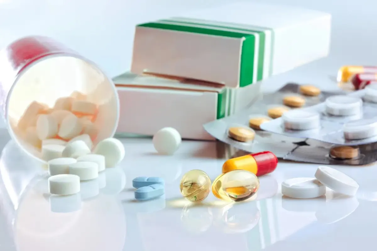 Cajas, blísters y comprimidos de medicamentos sobre una superficie blanca, ilustrando la adecuación de los formatos de antibióticos de la AEMPS