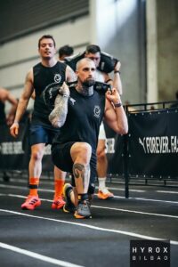 Deportista de CrossFit realizando lunges con sandbag en competición HYROX Bilbao sin dolor de cadera tras tratamiento podológico con plantillas personalizadas